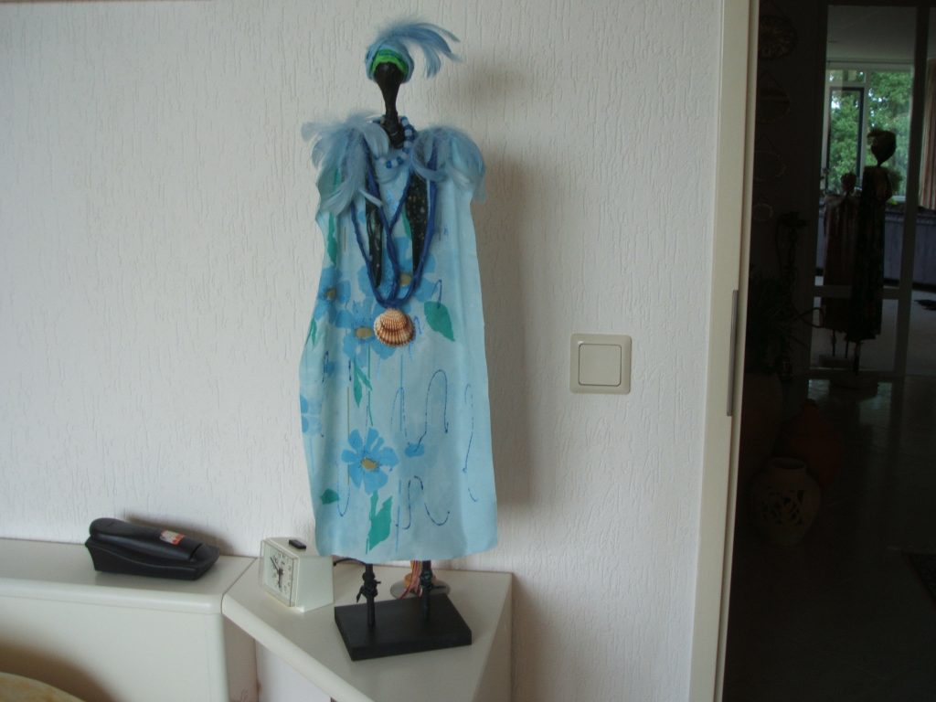 AFRIKAANSE VROUW Het lichaam is met blauwe stofje bekleed en bewerkt met textielverharder. Versierd met blauwe veren, kralen en een schelp. De hoogte van de pop is ongeveer 60 cm