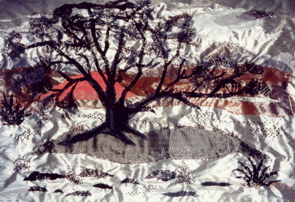 BOOM IN EEN WADI Applicatie. Ondergrond zilver stof met daarop lapjes, naaigaren, borduurgaren, kraaltjes en flitters. Ontwerp: Eerst een schets gemaakt naar een verzameling van foto's van bomen gemaakt op onze trips door Oman. Dit wandkleed behaalde een 1e prijs bij de David Barren Award 1994 in Oman.